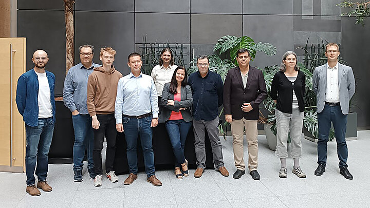A group of ten people stands in a large room facing the observer.