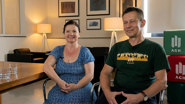 A woman and a man sit in a cozy room, facing the observer.