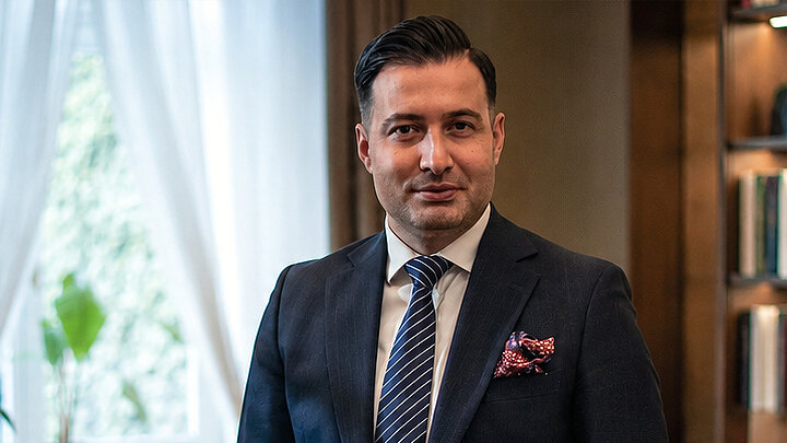 A man in a navy blue suit in a cozy office